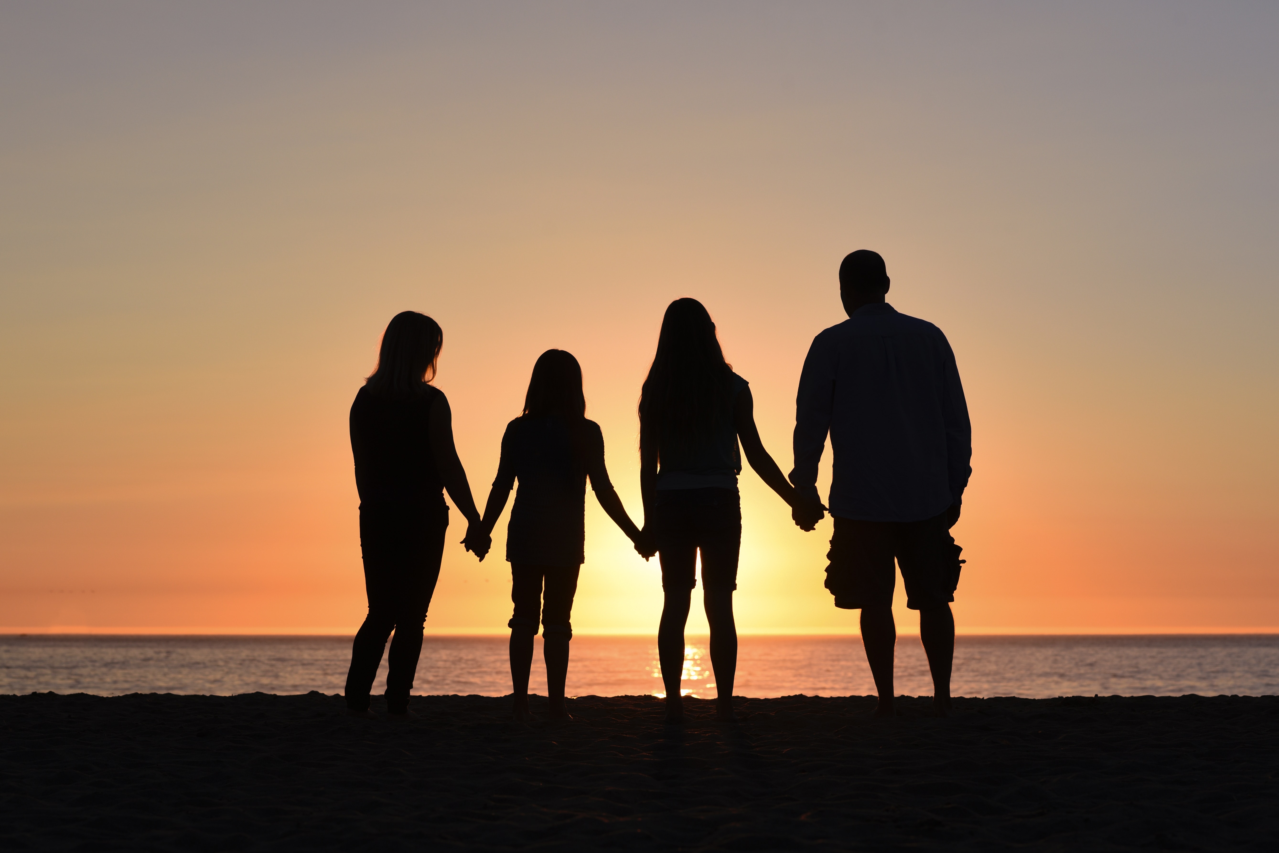 Family of four holding hands on a beach